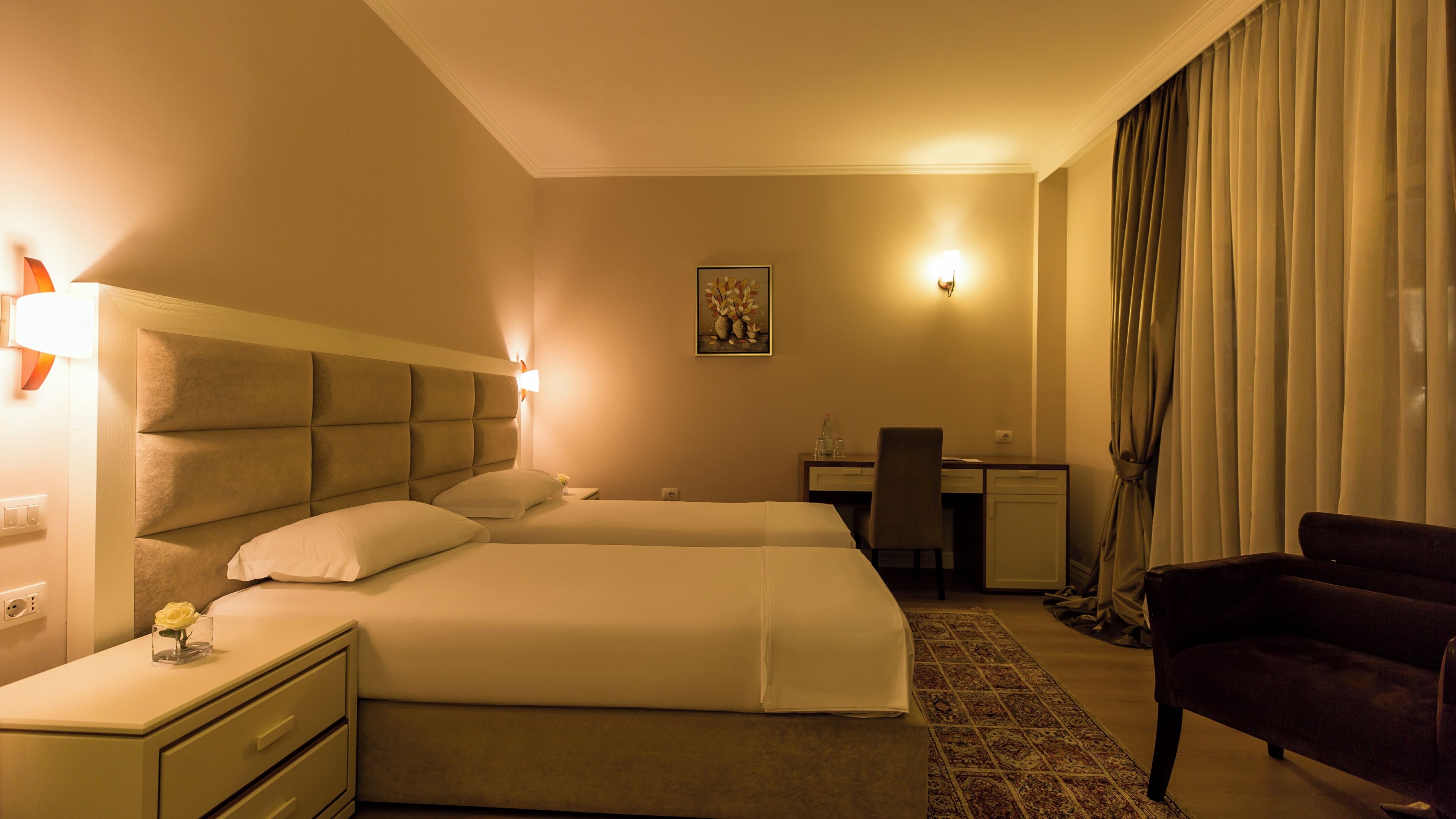 A hotel room with two beds, a desk, a chair, and a large window with curtains.