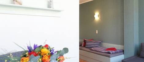 Una sala de estar moderna con un sofá, una mesita con un jarrón de flores y un estante montado en la pared con objetos decorativos.