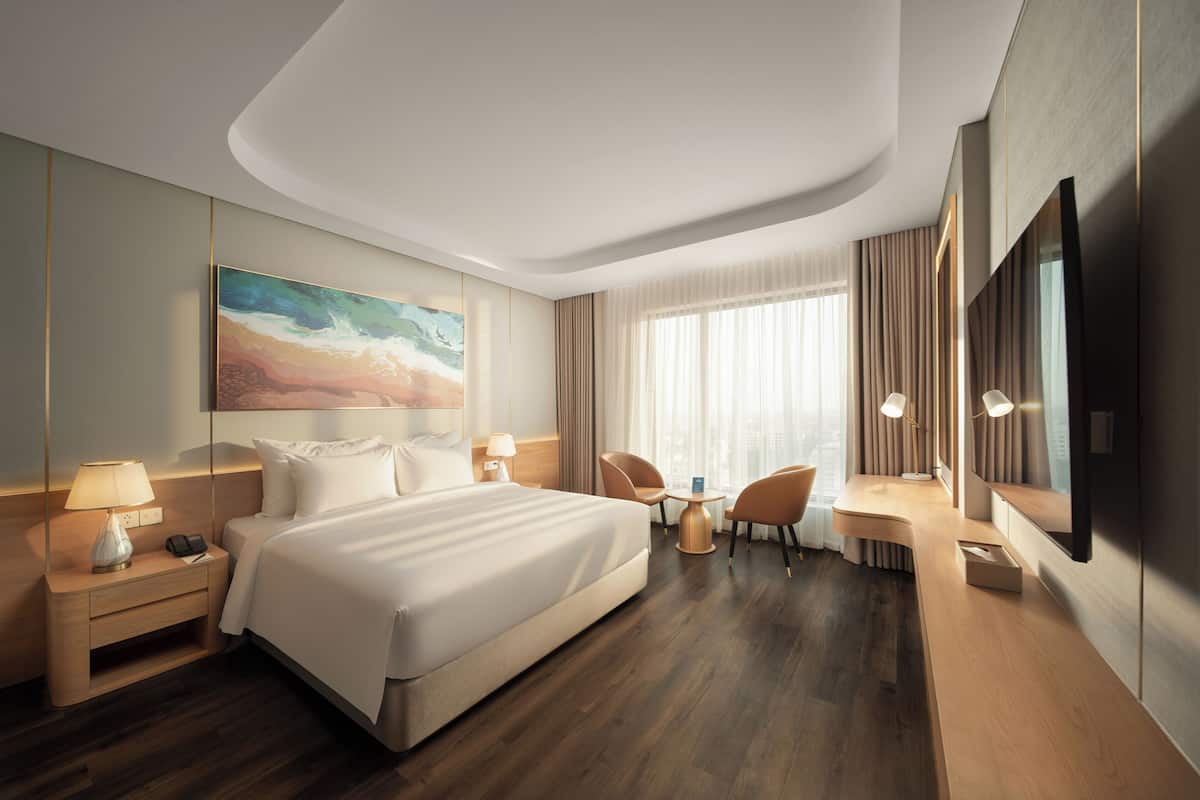 Une chambre d’hôtel avec un grand lit, des tables de chevet, un bureau avec des chaises, une télévision et un tableau au mur.