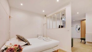 Een slaapkamer met een bed, een spiegel, een nachtkastje met een bloemenvaas, en uitzicht op de aangrenzende kamer.