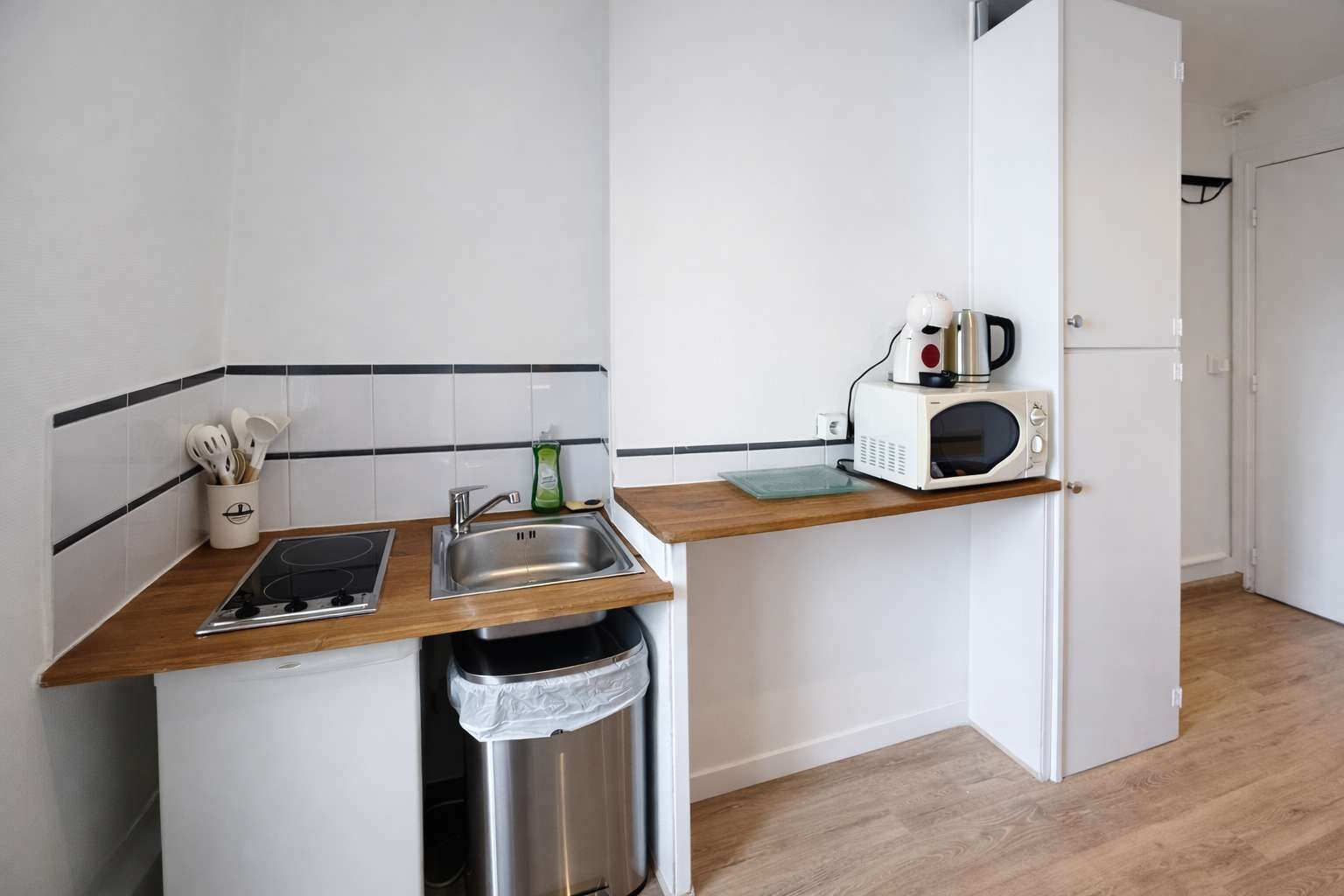 A compact kitchen with a sink, stove, microwave, and a trash bin.