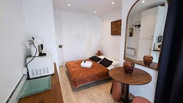 A compact hotel room with a bed, bedside table, and a small round table with a mirror.