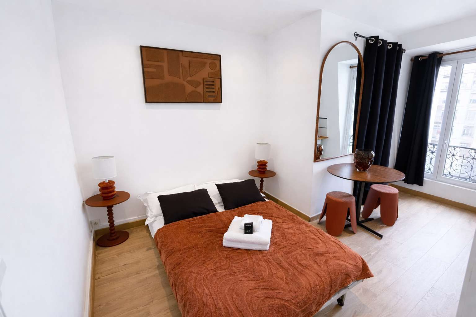 Ein Hotelzimmer mit Bett, kleinem Tisch, Stuhl, Spiegel und einem Fenster mit Vorhängen.