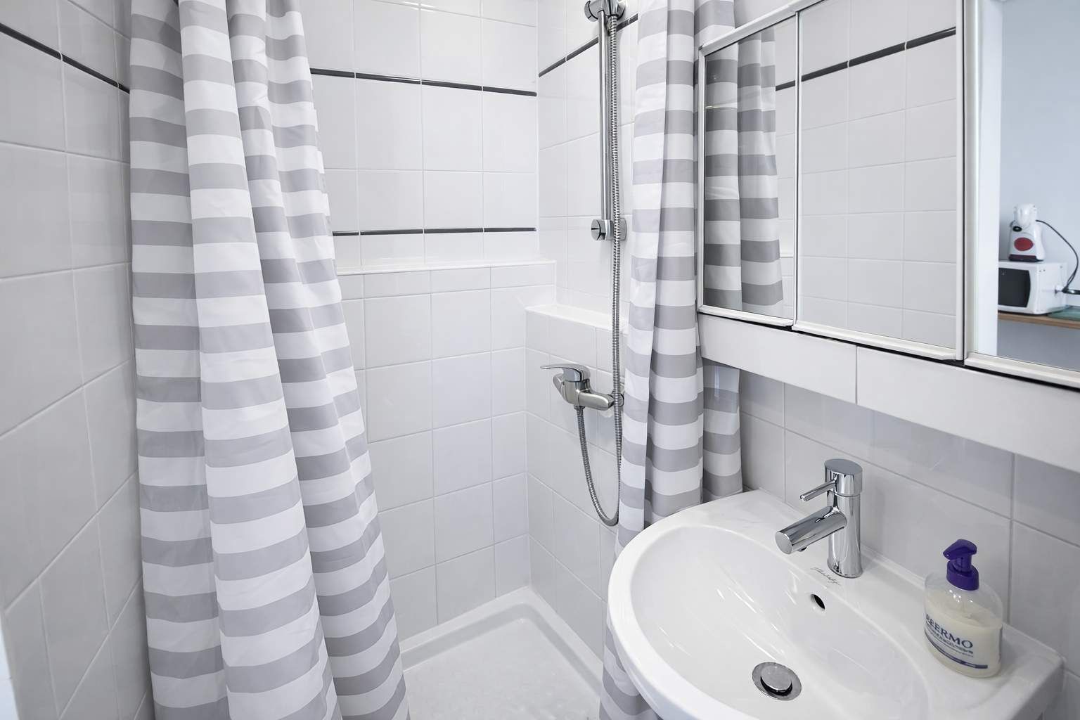 Ein modernes Badezimmer mit einem weißen Waschbecken, einem Spiegel und einer Dusche mit gestreiften Vorhängen.