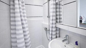 Une salle de bain moderne avec un lavabo blanc, un miroir et une douche avec des rideaux à rayures.