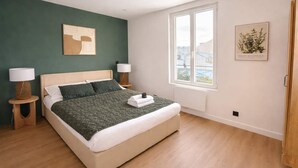 A bedroom with a bed, two bedside tables, a window, and a framed picture on the wall. - Charmant appartement a Aubervilliers, 4 personnes (Aubervilliers)