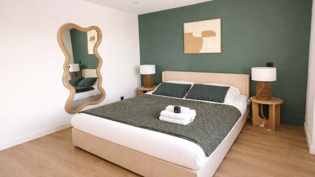 A modern bedroom with a large bed, two bedside tables, a mirror, and a wall art piece. - Charmant appartement a Aubervilliers, 4 personnes (Aubervilliers)