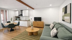 A modern living room with a green sofa, a dining table with chairs, a kitchen area with white cabinets, and a TV on a wooden cabinet. - Charmant appartement a Aubervilliers, 4 personnes (Aubervilliers)