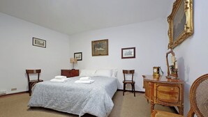 Ein Schlafzimmer mit einem Bett, zwei Stühlen, einer Kommode und drei gerahmten Bildern an der Wand.