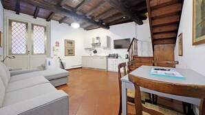 Ein gemütliches Wohnzimmer mit Sofa, Esstisch mit Stühlen, einer Küchenzeile mit Schränken und einem Fernseher, sowie einer Treppe.