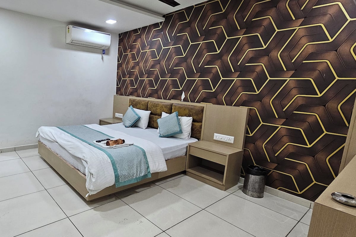 A bedroom with a bed, bedside tables, a TV, an air conditioner, and a patterned wall.