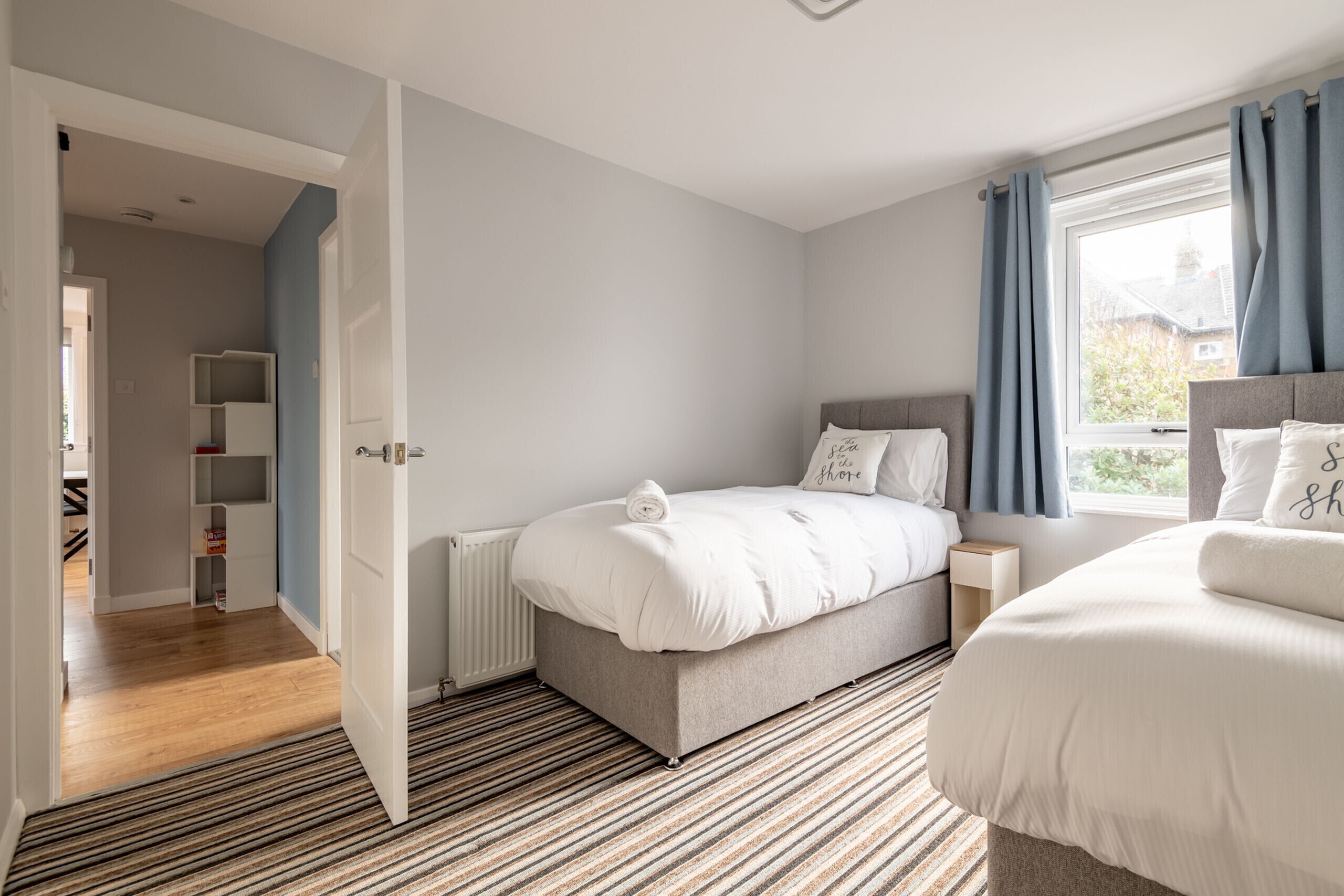 A bedroom with a bed, a bedside table, a window with curtains, and a view of the outside.