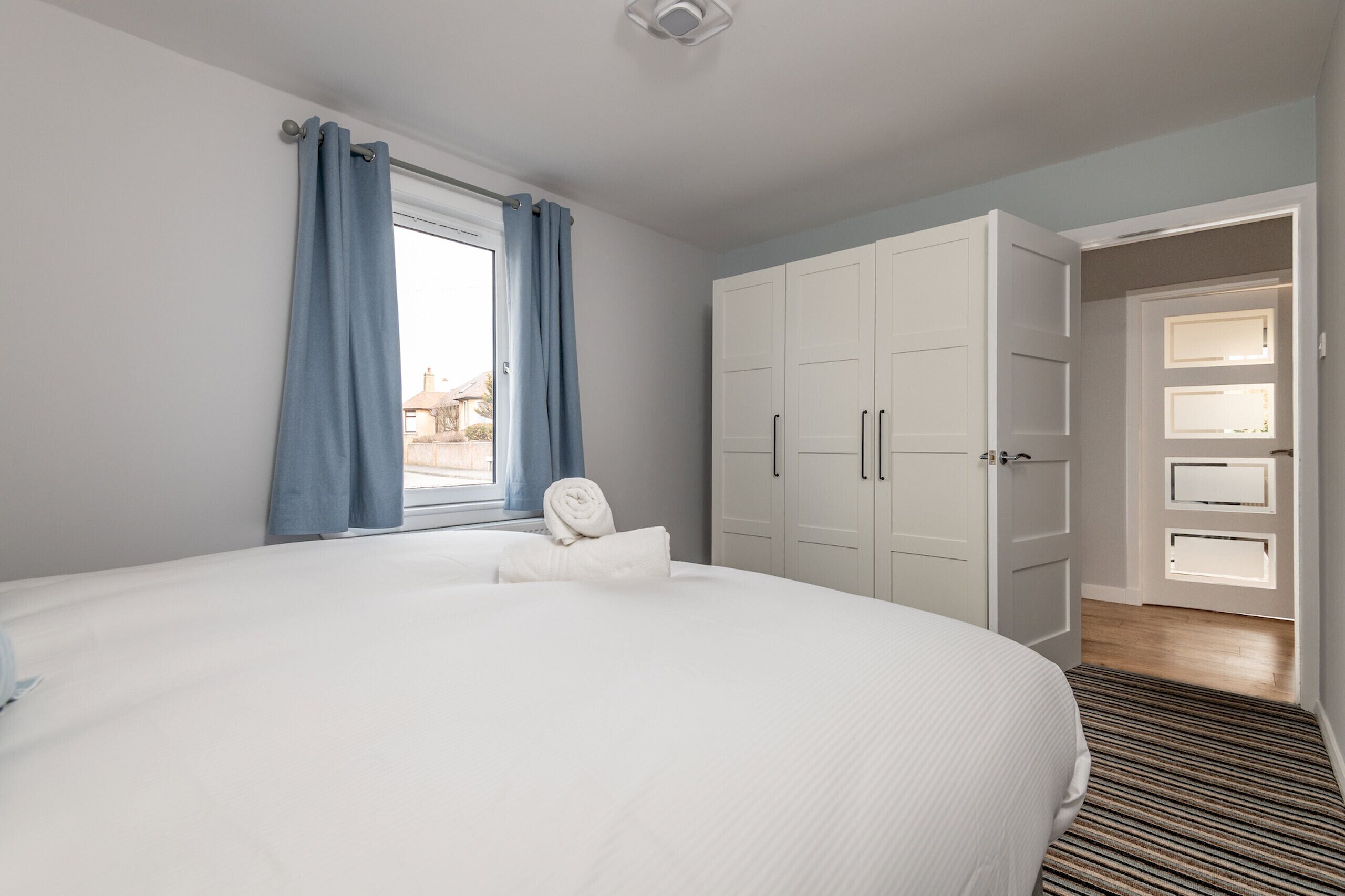 A bedroom with a large bed, a wardrobe, and a window with curtains.