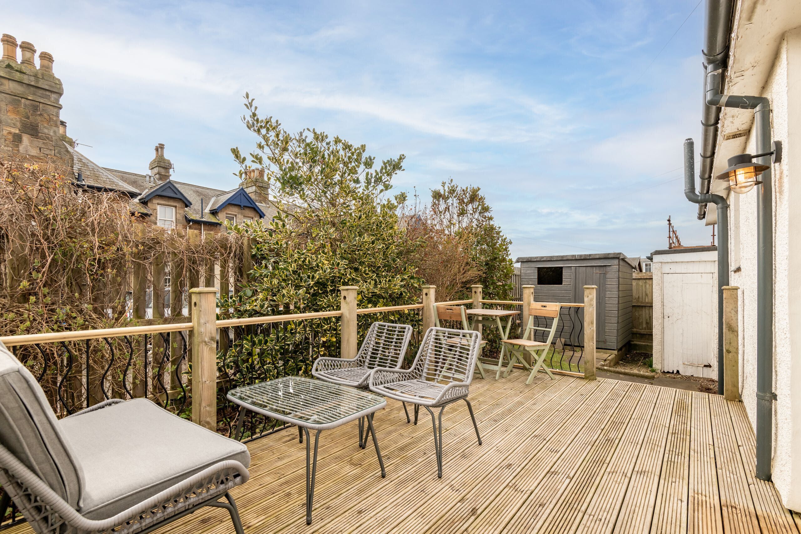 A wooden deck with metal chairs and a table, surrounded by a wooden fence and greenery.
