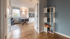 A modern interior with a dining area, kitchen, and a white shelving unit against a blue wall. - Admiralty Lane (No 4) (Elie)