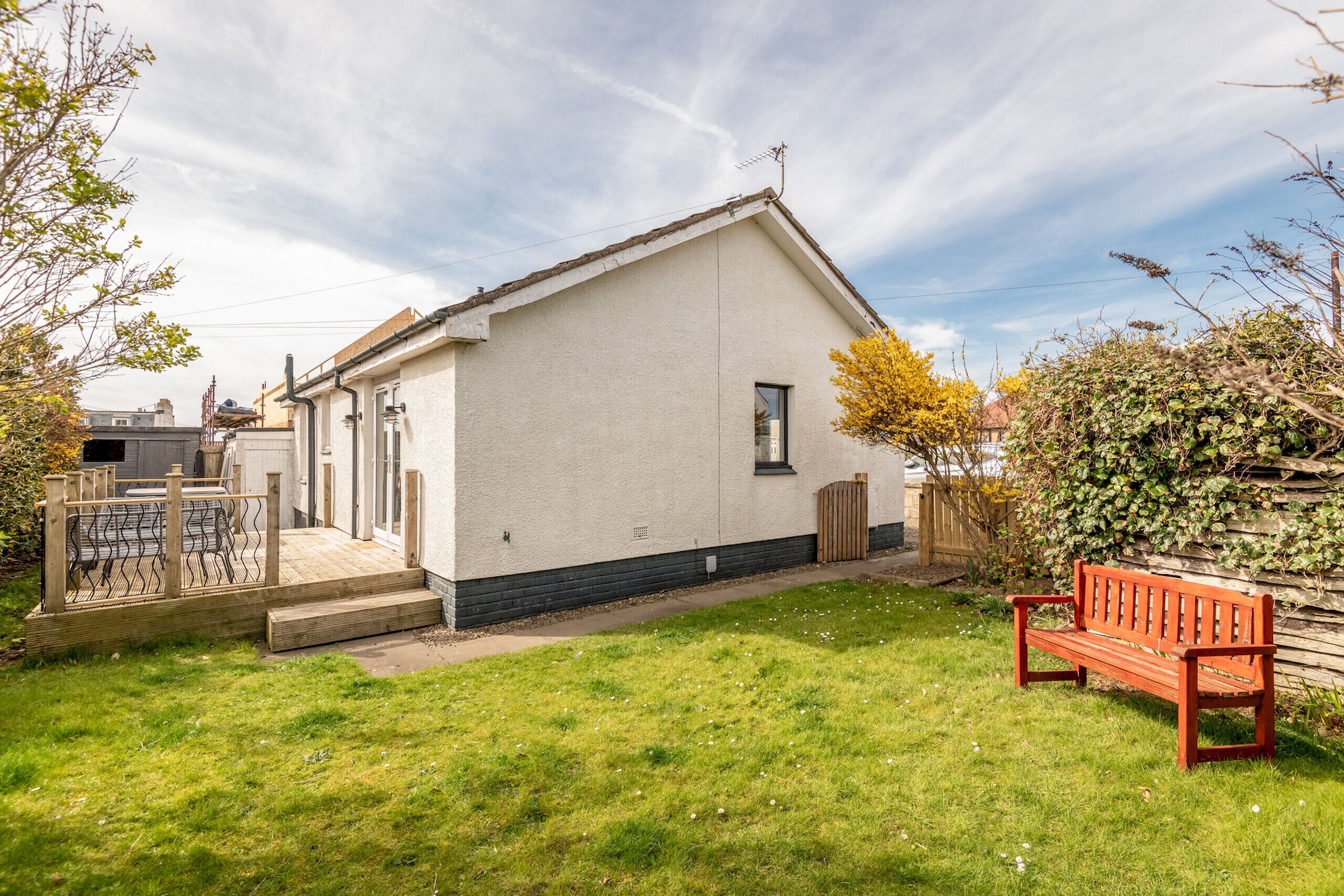 Een laag gebouw met een plat dak, een klein raam en een houten bankje in de voortuin.