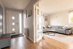 A room with a grey sofa, a small round table, and a wooden floor. - Admiralty Lane (No 4) (Elie)