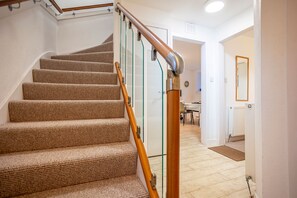 A carpeted staircase with wooden handrails, leading to a room with a white radiator and a door. - Admiralty Square (No 1) | Elie (Elie)
