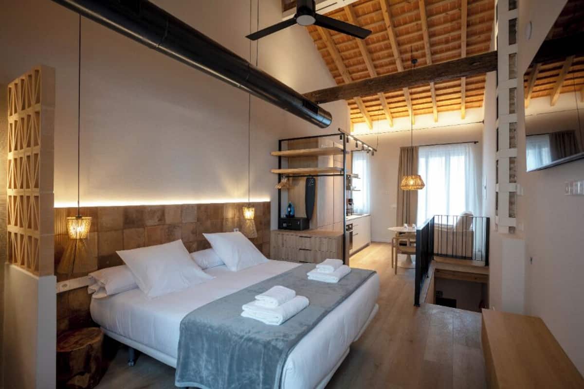 A modern hotel room with a large bed, a desk, and a kitchenette.