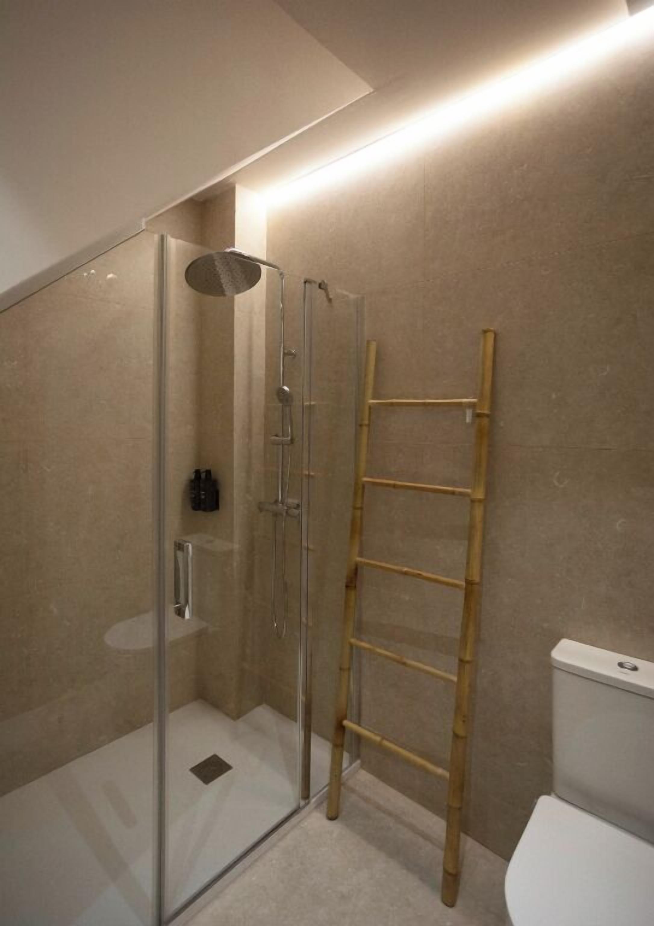 Un baño moderno con ducha de vidrio, escalera de madera y un inodoro.