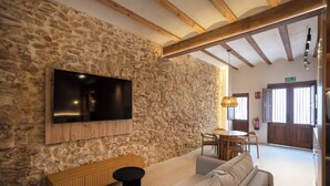 A stone-walled living room with a flat-screen TV, a sofa, a wooden bench, and a small table. - Mon Suites San Pedro (Valencia)