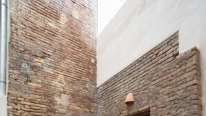 A small, enclosed outdoor space with a stone wall, a round table, two wicker chairs, and a window with a view of the sky. - Mon Suites San Pedro (Valencia)