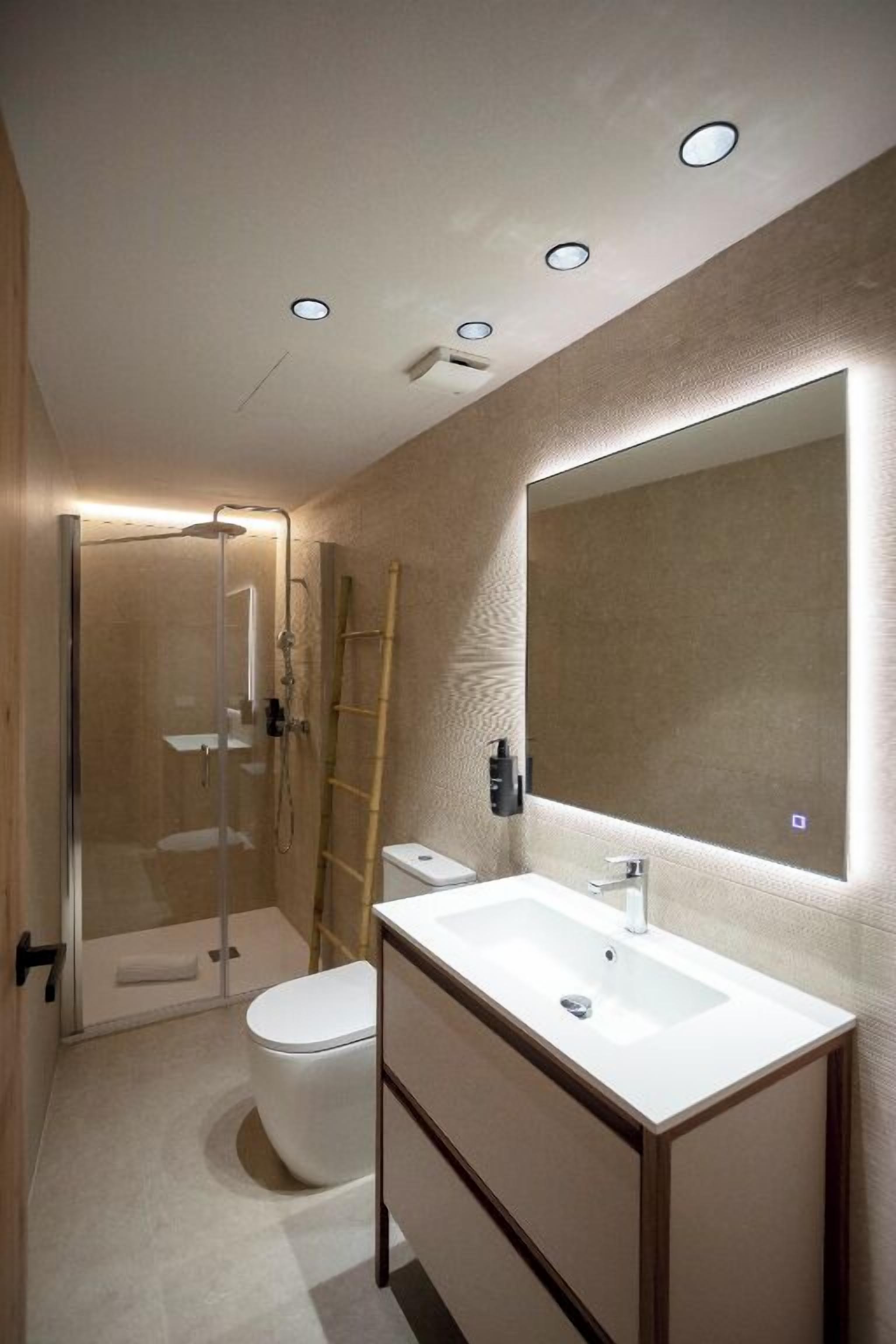 Un baño moderno con cabina de ducha de vidrio, inodoro, lavabo con espejo e iluminación empotrada en el techo.