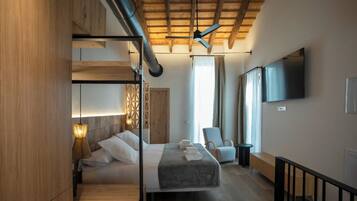 A modern hotel room with a bunk bed, a desk, a chair, a TV, and a large window.
