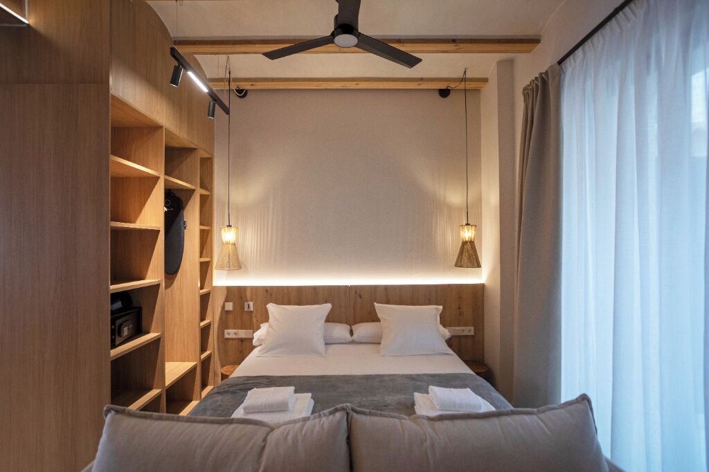 Une chambre d’hôtel moderne avec un grand lit, des étagères en bois et des luminaires suspendus.