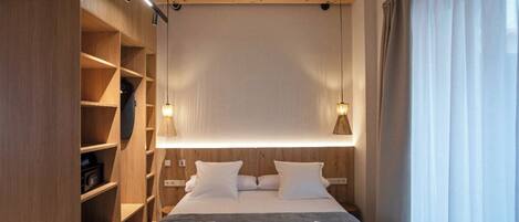 Une chambre d’hôtel moderne avec un grand lit, des étagères en bois et des luminaires suspendus.