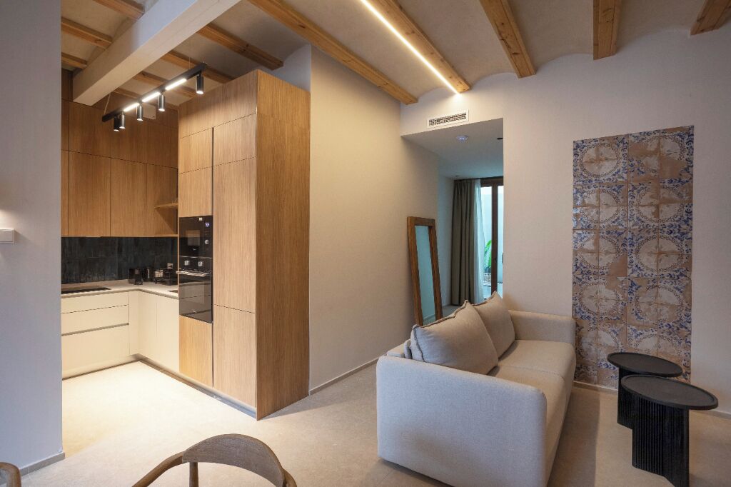 Una cocina moderna con armarios de madera y horno empotrado. En la sala de estar, hay un sofá y una pequeña mesa.