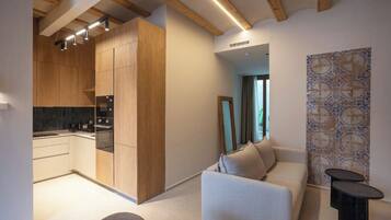 Una cocina moderna con armarios de madera y horno empotrado. En la sala de estar, hay un sofá y una pequeña mesa.