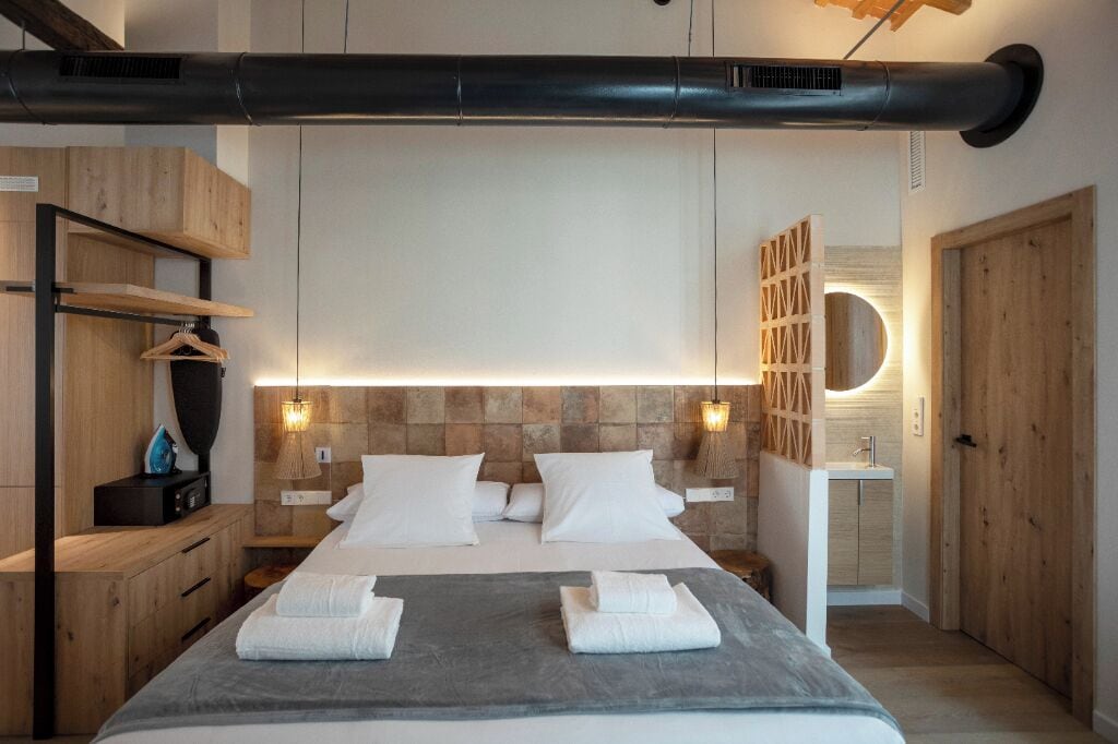 A modern hotel room with a large bed, wooden headboard, and a built-in circular light fixture.