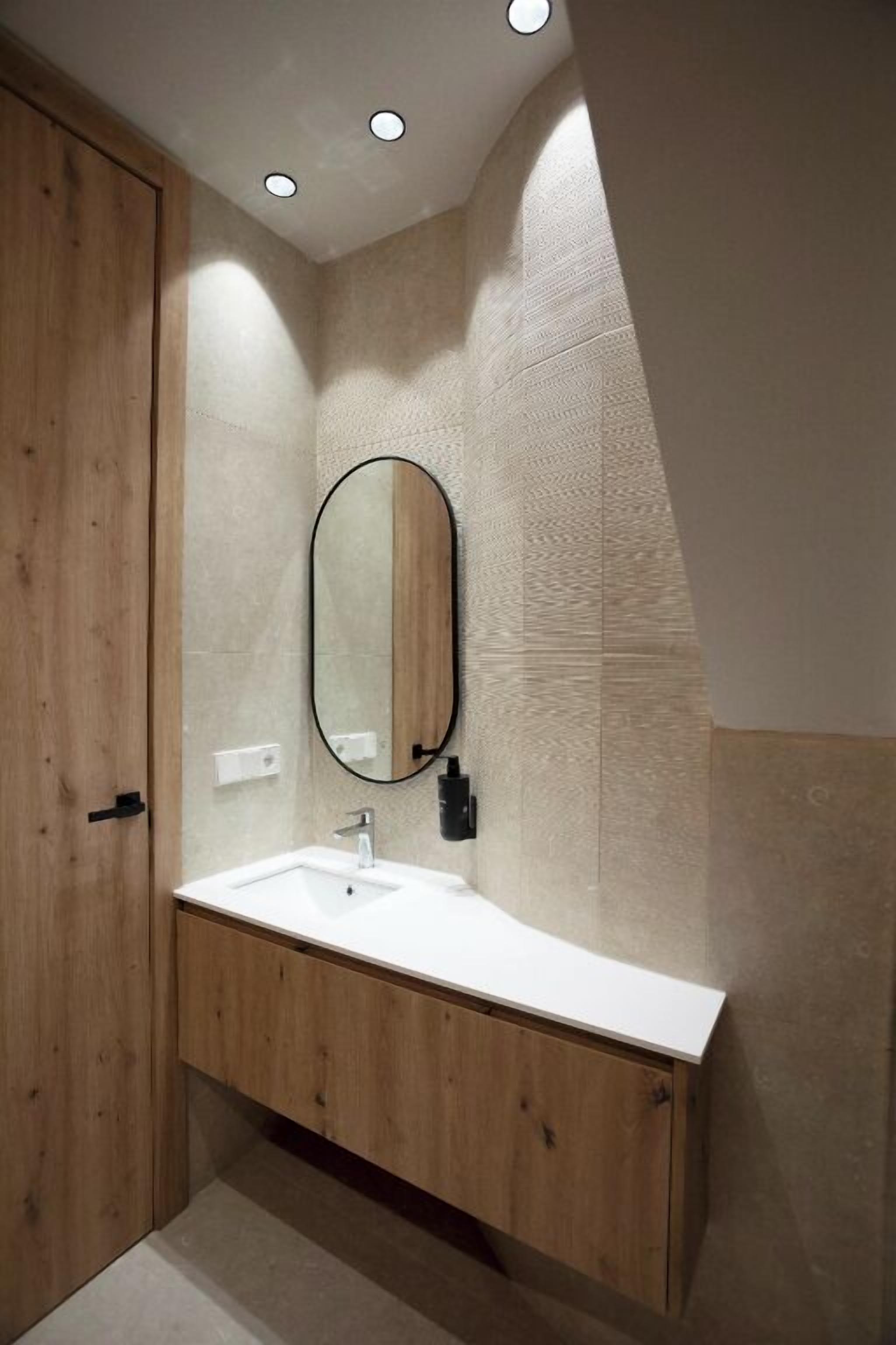 Un baño moderno con tocador de madera, lavamanos blanco y un espejo grande.