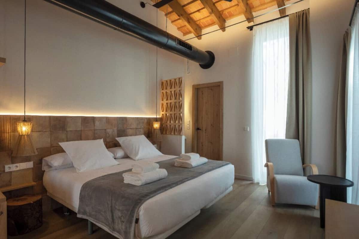 A modern bedroom with a large bed, a wooden headboard, a chair, and a small table.