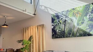 A modern living room with a sofa, a dining table with chairs, a large window, and a tropical plant. - NIKAIDO SKY TERRACE (Tokyo)