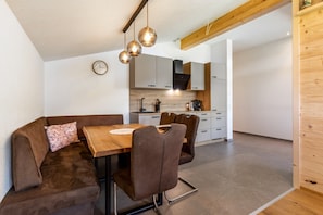 A modern kitchen with white cabinets, a wooden ceiling, and a dining area with a wooden table and brown chairs. - Your Grubgut Getaway – Vacation with Mountain Views (Taxenbach)