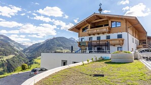 Un edificio de dos plantas con balcón, una estructura pequeña adosada y vistas a montañas.