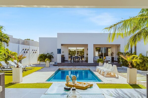 Uma área de piscina moderna com espreguiçadeiras, mesa de bilhar e espaço de refeições com mesas e cadeiras.