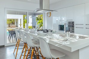 Une cuisine moderne dotée d’un îlot central, de meubles blancs et donnant sur une terrasse extérieure.