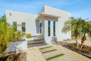 Uma casa moderna de dois andares com telhado plano, janelas amplas e escadaria de concreto que leva à entrada.