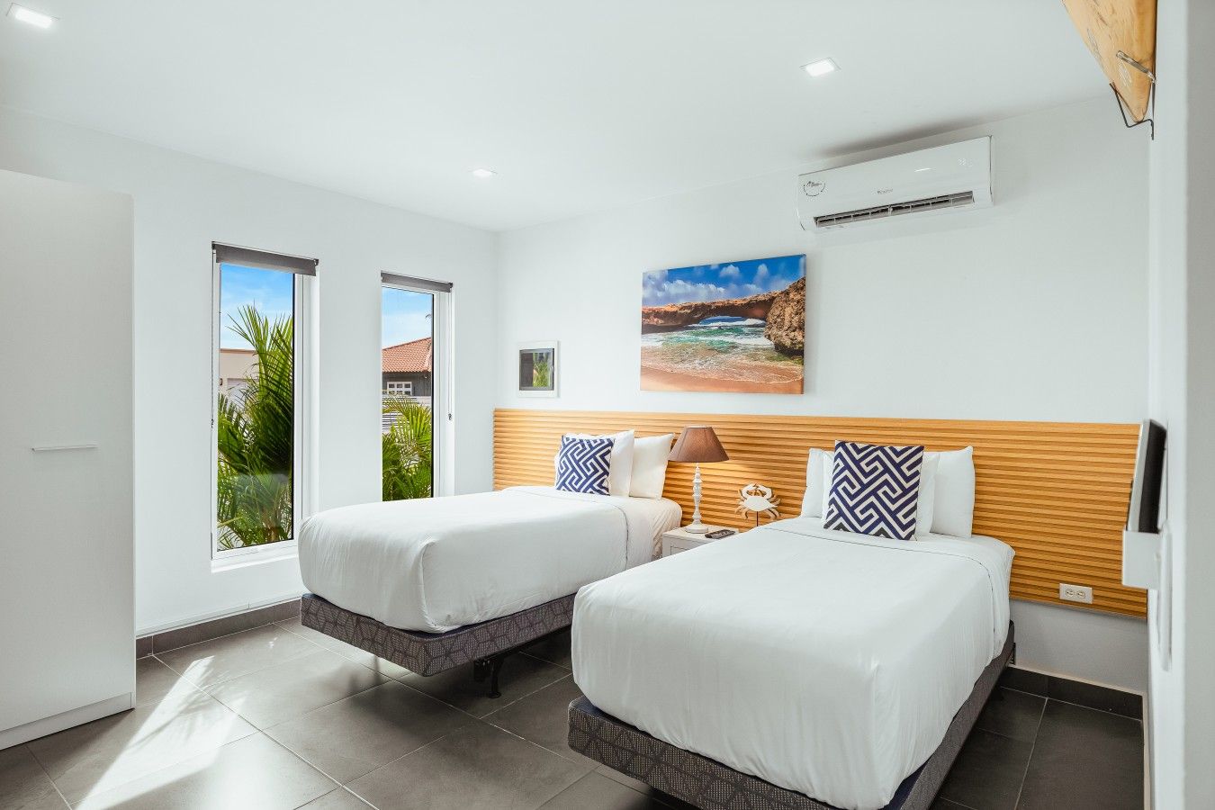 Une chambre d’hôtel avec deux lits, une fenêtre, un climatiseur et un tableau au mur.