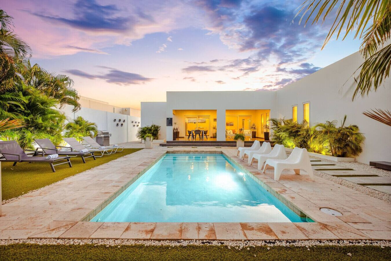 Una piscina con sillas de descanso, un patio y un edificio con entrada abierta.