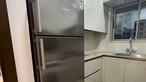 A kitchen with a stainless steel Bosch refrigerator, beige cabinets, a window, and a sink.