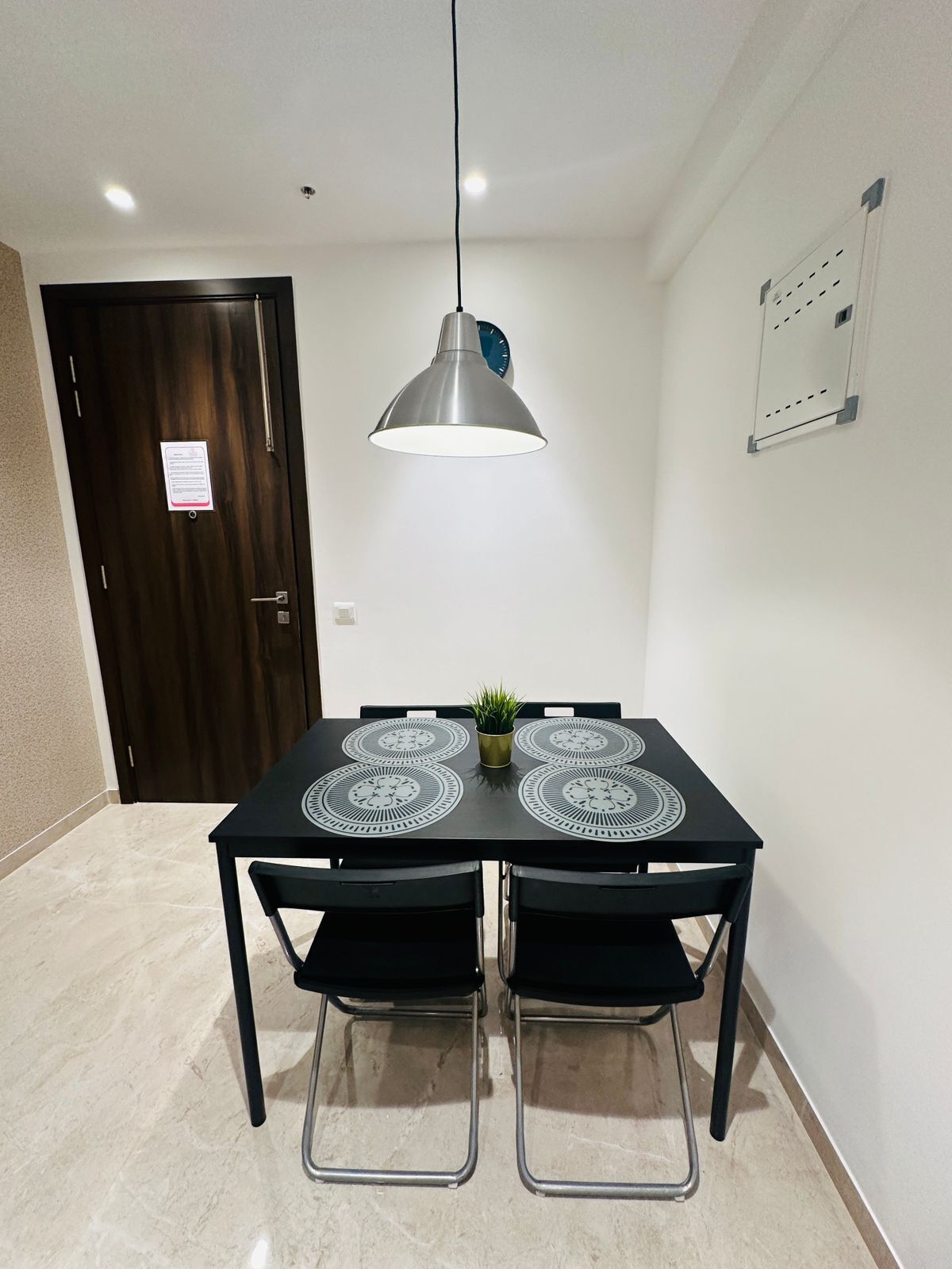 A dining area with a table and chairs, a pendant light, a door, and a wall-mounted board.