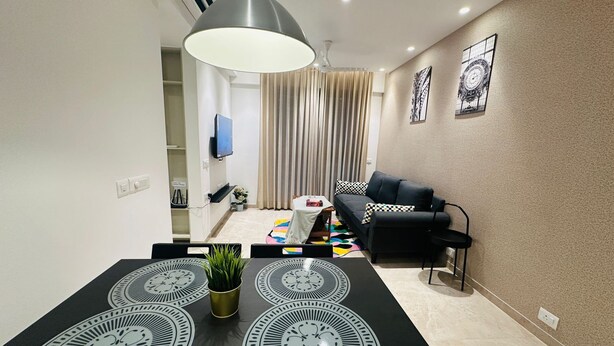 A modern living room with a black sofa, a dining table with a unique black and white table runner, and a large pendant light.