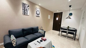 A modern living room with a black sofa, a small coffee table, and a dining area with a table and chairs.