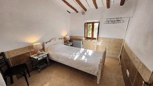 Une chambre à coucher comprenant un lit, une table de chevet, une lampe, une chaise, un radiateur et une fenêtre donnant sur un paysage verdoyant.