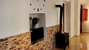 Une pièce avec une horloge au mur, une cheminée avec un téléviseur et un radiateur noir.