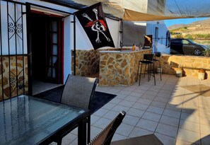 En udendørs terrasse med en stenvæg, et glasbord og et flag.